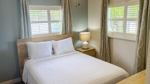 Cama bem arrumada com roupa de cama branca, cabeceira de madeira e mesa de cabeceira com abajur.
