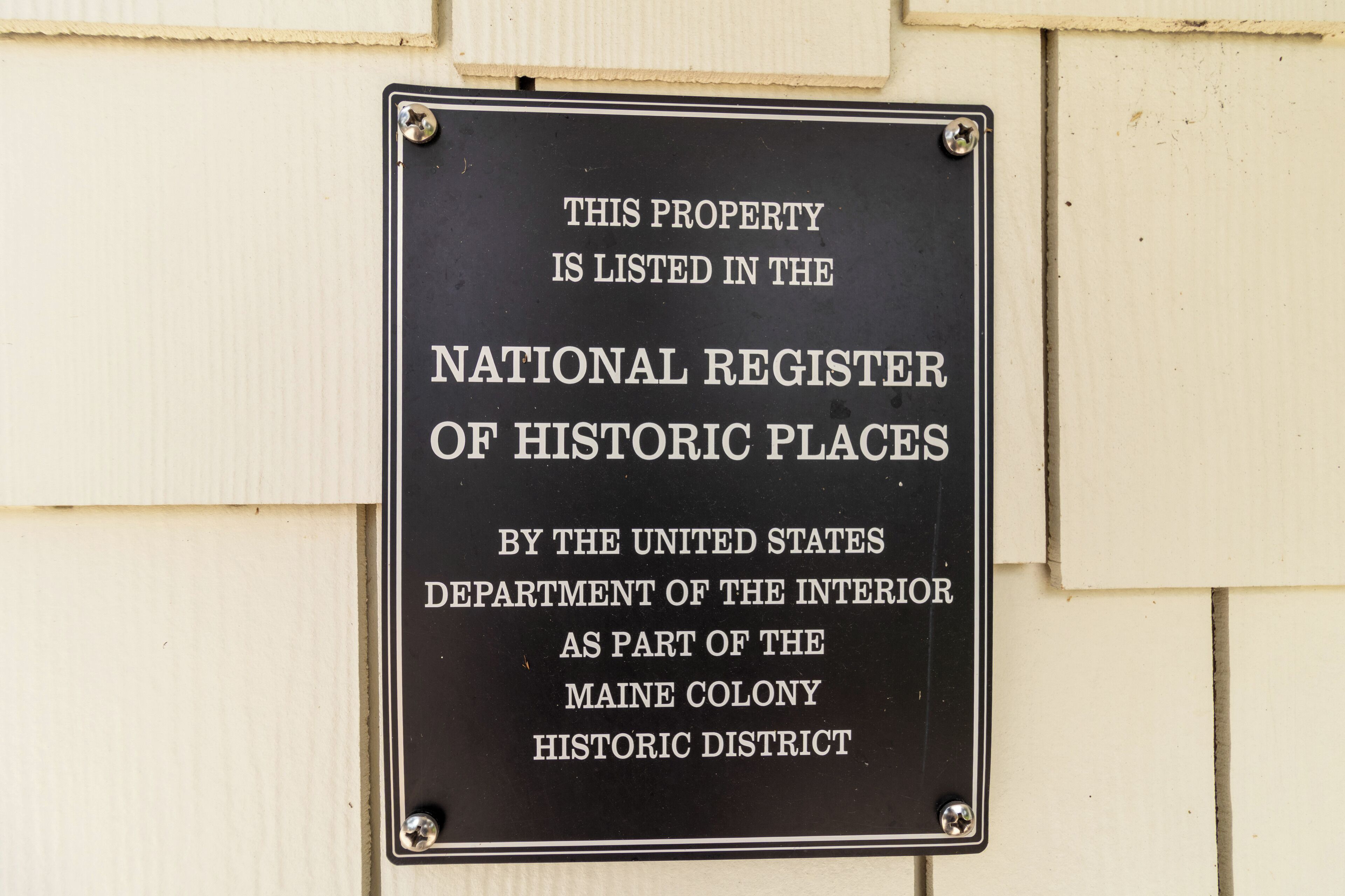A black sign with white lettering on a beige wall, indicating the property is listed in the National Register of Historic Places.