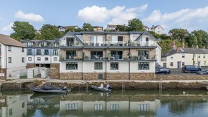Un edificio moderno de dos pisos con balcones, fachada de piedra y un canal en primer plano.