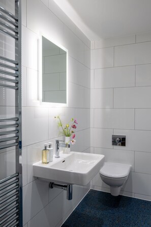 A modern bathroom with a white sink, mirror, and toilet. - 3 The Boatyard - sleeps 8 guests  in 4 bedrooms (Kingsbridge)