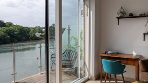 Una habitación moderna con un amplio ventanal corredera que da a un balcón con vistas a un río.