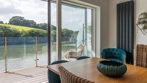Una habitación moderna con un gran ventanal corredera que da a un balcón con vistas a un cuerpo de agua y vegetación.