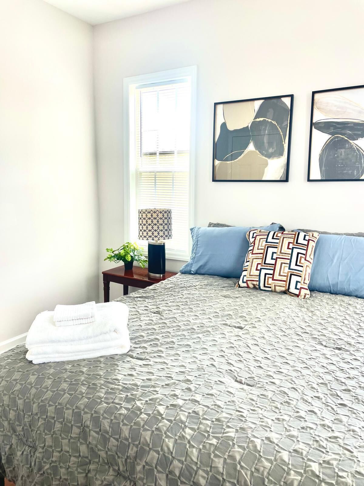 Una cama bien hecha con un edredón estampado, una almohada azul y una almohada decorativa con diseño geométrico.