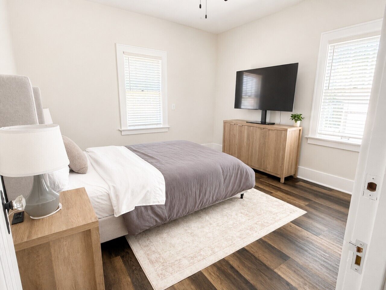 A bedroom with a bed, bedside table, lamp, TV, and a small plant.