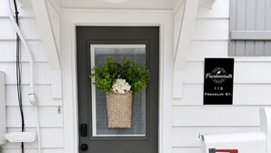 A front door with a dark gray color, a welcome mat, a basket with flowers, a mailbox, and a sign indicating the address. - Franklin Haus - Frankenmuth Vacation Homes (Frankenmuth)