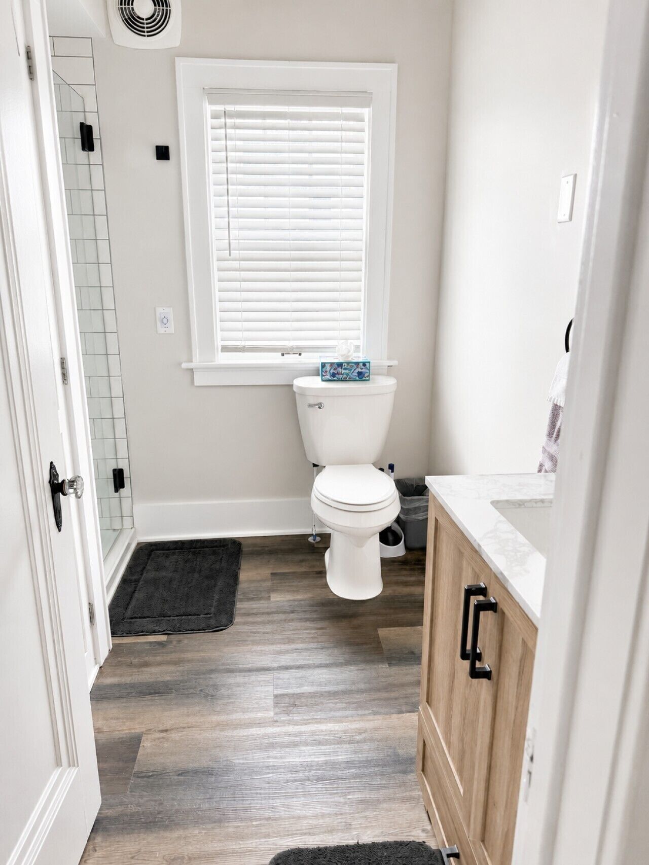 Un baño con inodoro, ventana con persianas, zona de ducha y mueble de madera.
