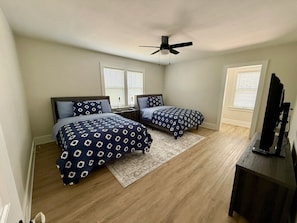 Un dormitorio con dos camas, ventilador de techo, un mueble para televisor y una ventana con persianas.