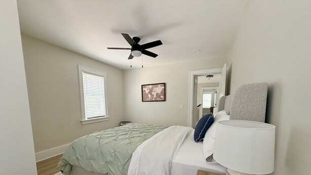 A bedroom with a bed, a ceiling fan, a bedside lamp, a window, and a door. - Franklin Haus - Frankenmuth Vacation Homes (Frankenmuth)
