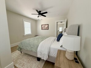 Una camera da letto con un letto, una ventola a soffitto, una lampada da comodino, una finestra e una porta.