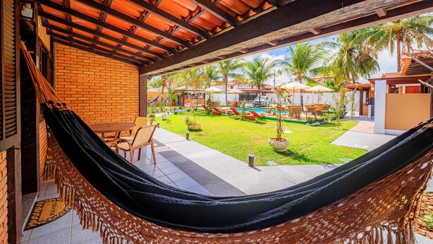 A hammock under a wooden ceiling with a view of a well-maintained garden and pool area. - Brisas do Oceano Lofts (Buzios)