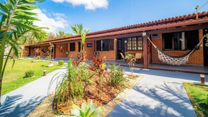A two-story building with a red-tiled roof, a hammock, and a well-maintained garden with various plants. - Brisas do Oceano Lofts (Buzios)