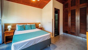 A bedroom with a bed, wooden headboard, nightstands, a ceiling fan, and a wardrobe. - Brisas do Oceano Lofts (Buzios)