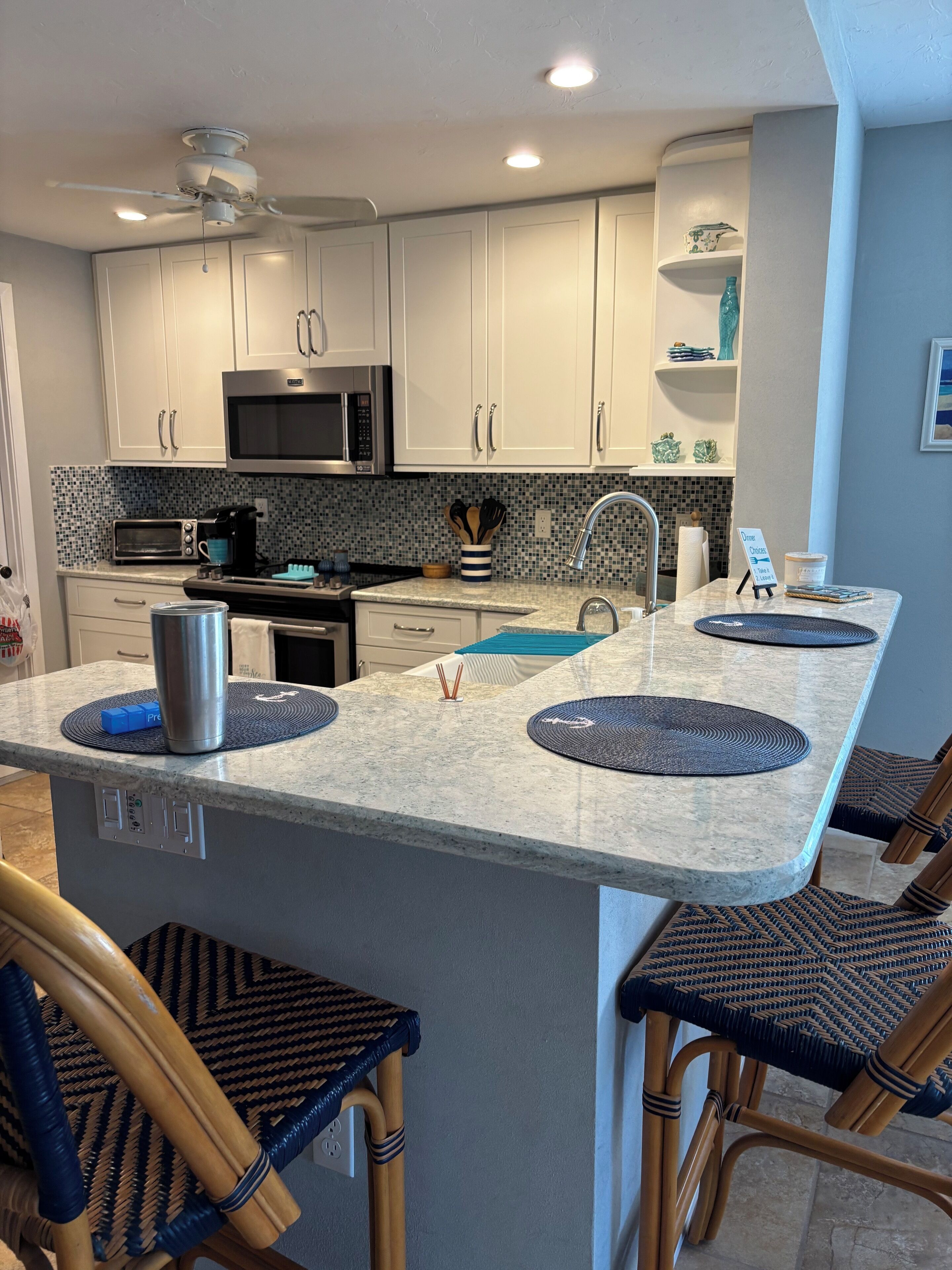 Een moderne keuken met witte kasten, een centraal eiland met zitplaatsen, een magnetron en een broodrooster.