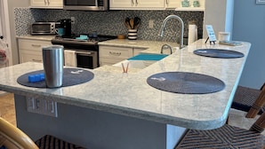 A modern kitchen with white cabinets, a central island with seating, a microwave, and a toaster. - Newly renovated  2 bedroom condo on siesta key beach…steps to private beach. (Siesta Key)