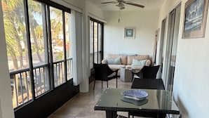 A spacious room with a glass table, wicker chairs, a ceiling fan, and large windows offering a view of palm trees and a street. - Newly renovated  2 bedroom condo on siesta key beach…steps to private beach. (Siesta Key)
