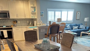 A dining area with a wooden table, wicker chairs, and a tray with decorative items. - Newly renovated  2 bedroom condo on siesta key beach…steps to private beach. (Siesta Key)