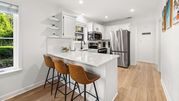 A modern kitchen with white cabinetry, stainless steel appliances, and a large island with bar stools. - Fully renovated! Great rates on a charming 2/2 steps from the beach! (Santa Rosa Beach)