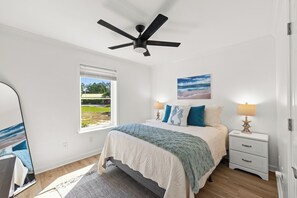 A bedroom with a bed, a nightstand, a lamp, a ceiling fan, a window with a view, and a painting on the wall. - Fully renovated! Great rates on a charming 2/2 steps from the beach! (Santa Rosa Beach)