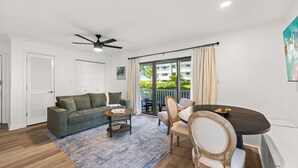 A living room with a sofa, coffee table, and dining table, a ceiling fan, and a view through a glass door. - Fully renovated! Great rates on a charming 2/2 steps from the beach! (Santa Rosa Beach)