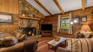 A cozy log cabin interior with a stone fireplace, leather furniture, and a television. - Almost Heaven – Porch Swing Mountain Getaway (Franklin)