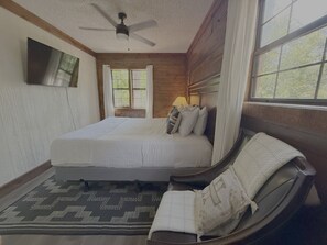 A bedroom with a bed, a ceiling fan, a window with curtains, and a television on the wall.
