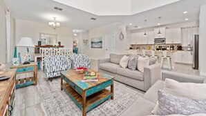Ein geräumiges Wohnzimmer mit grauem Sofa, einem Couchtisch und gemusterten Sesseln.