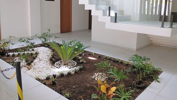 Un intérieur moderne avec un jardin central, un escalier doté de rampes en verre et une porte portant l’inscription « 10 ».