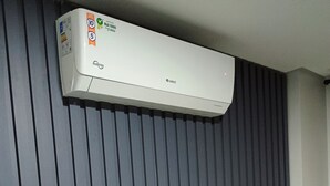 Un salon moderne avec un téléviseur à écran plat posé sur une console blanche, une plante en pot et un climatiseur fixé au mur.