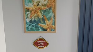 Un petit coin repas avec deux chaises bleues, une table blanche et un tableau encadré représentant des étoiles de mer, accroché au mur.