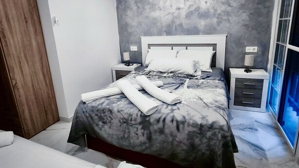 A modern bedroom with a large bed, a wooden wardrobe, and a nightstand with a lamp. - Airbhouse Prívate Rooms & Triana (Seville)