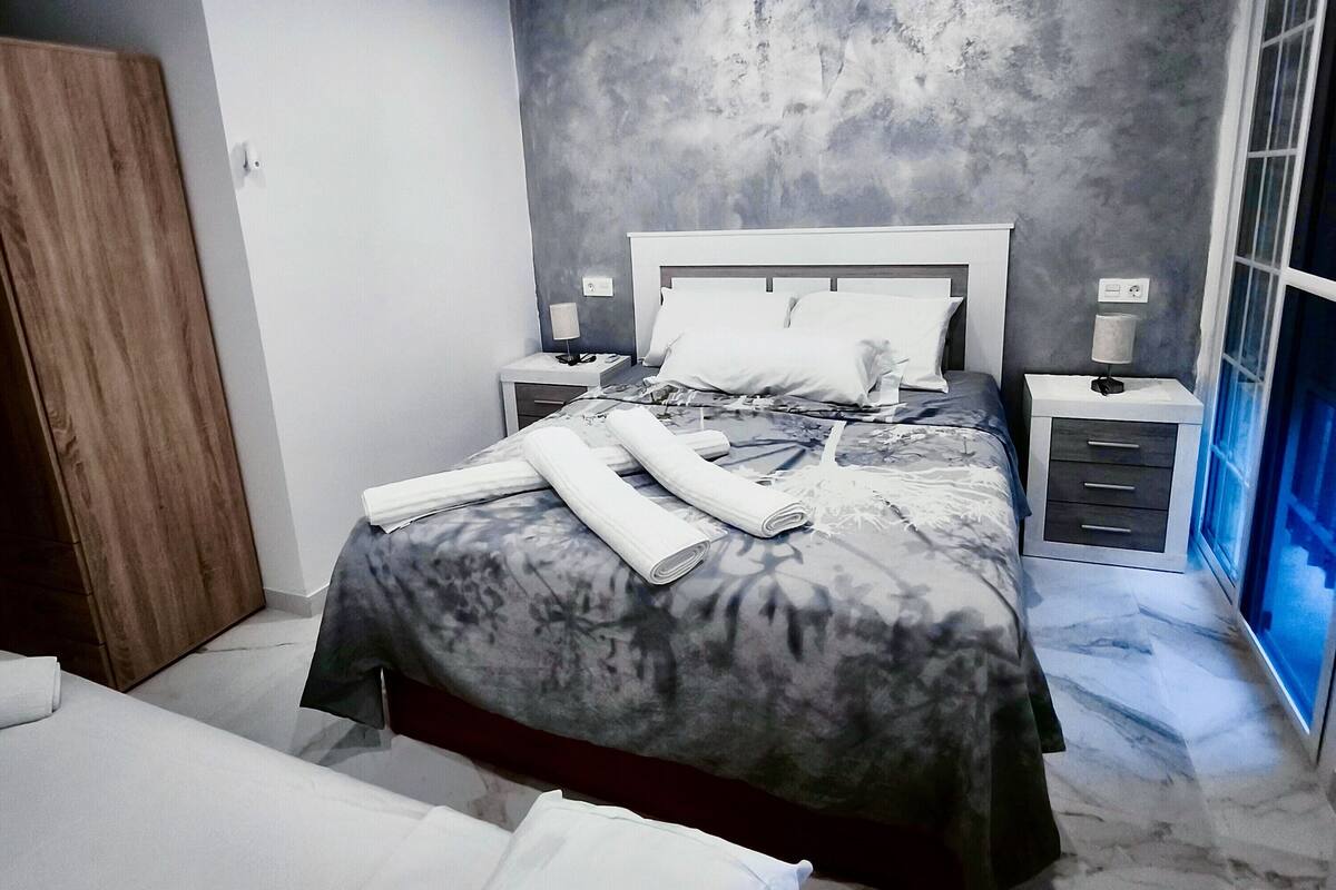 A modern bedroom with a large bed, a wooden wardrobe, and a nightstand with a lamp.