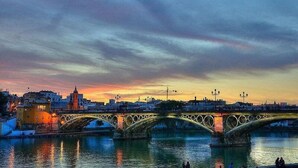 A bridge with multiple arches over a body of water, reflecting city lights and buildings. - Airbhouse Prívate Rooms & Triana (Seville)