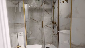 A modern bathroom with a glass-enclosed shower, white marble tiles, and gold fixtures. - Airbhouse Prívate Rooms & Triana (Seville)