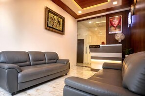 A reception area with a reception desk, a sofa, and a wall-mounted fan. - Hotel R K Residency Near Bihariji Mandir (Mathura)
