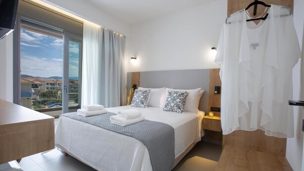 Una habitación de hotel moderna con una cama grande, una mesita de noche de madera, una mesilla auxiliar y vistas al exterior a través de un ventanal.