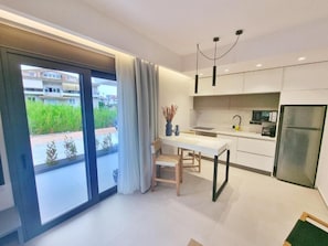 A modern kitchen with a dining area, large windows, and a view of greenery outside. - Achillion Suites (Lefkada)