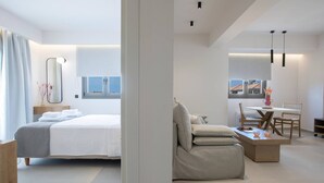A modern hotel room with a bed, a seating area with a table and chairs, and a view of the outside. - Achillion Suites (Lefkada)