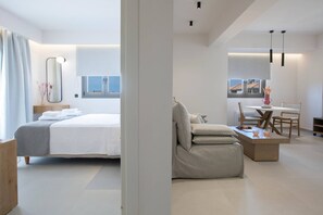 A modern hotel room with a bed, a seating area with a table and chairs, and a view of the outside. - Achillion Suites (Lefkada)