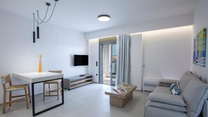 Una sala de estar moderna con un sofá blanco, una mesa de centro, una mesa de comedor con sillas, un televisor de pantalla plana y un ventanal con cortinas.