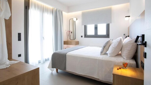 A modern bedroom with a large bed, bedside tables, a mirror, and a window. - Achillion Suites (Lefkada)