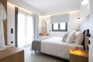 A modern bedroom with a large bed, bedside tables, a mirror, and a window. - Achillion Suites (Lefkada)