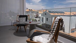 Un balcón con mesa y sillas, vistas a edificios cercanos y paneles solares en los tejados.