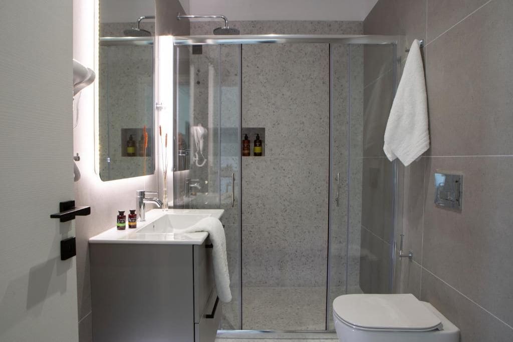Un bany modern amb plat de dutxa envoltat de vidre, un lavabo blanc i un vàter.