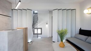 A modern interior with a reception desk, a staircase, and a seating area with a sofa and a table. - Achillion Suites (Lefkada)