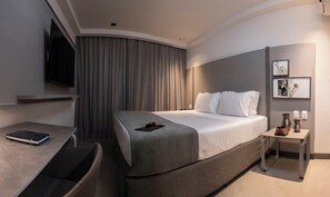 Une chambre d’hôtel moderne équipée d’un grand lit, d’un bureau, d’une chaise, d’une télévision et d’une table de chevet avec une lampe.