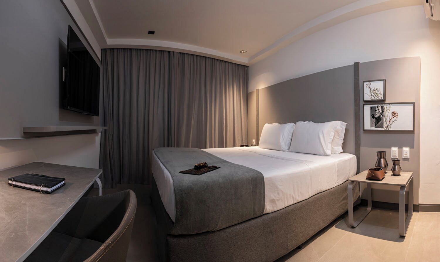 Ein modernes Hotelzimmer mit einem großen Bett, einem Schreibtisch, einem Stuhl, einem Fernseher und einem Nachttisch mit Lampe.
