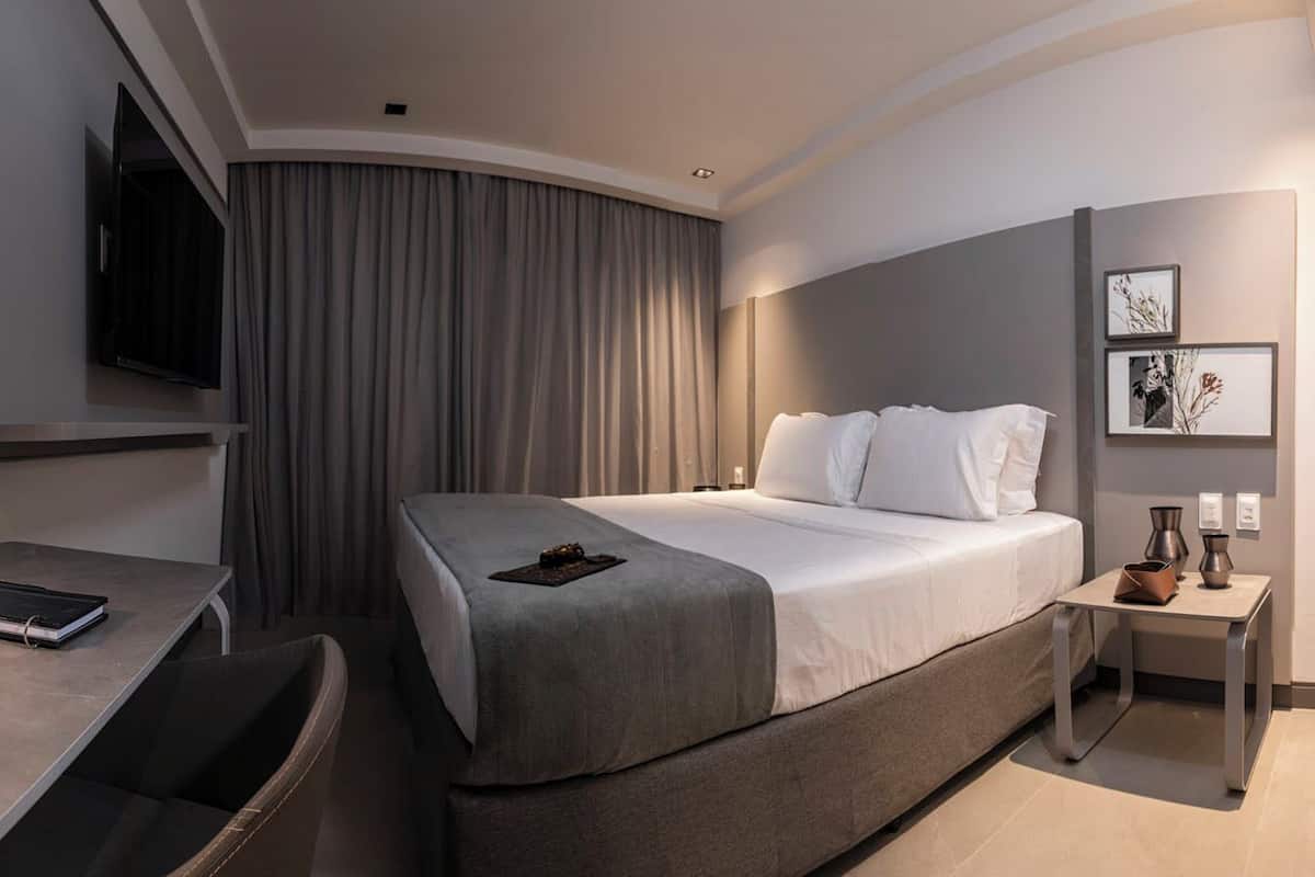Ein modernes Hotelzimmer mit einem großen Bett, einem Schreibtisch, einem Stuhl, einem Fernseher und einem Nachttisch mit Lampe.