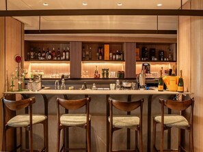 Un espace bar doté de tabourets en bois, d’un comptoir orné de diverses bouteilles et de verres, et d’une ambiance bien éclairée.