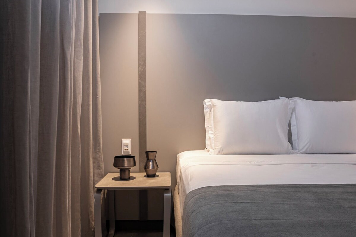 Une chambre d’hôtel avec un lit, une table de chevet, une lampe et un rideau.