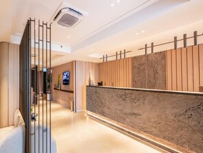 Un espace d’accueil d’hôtel comprenant un comptoir de réception, un téléviseur et un aménagement intérieur moderne.